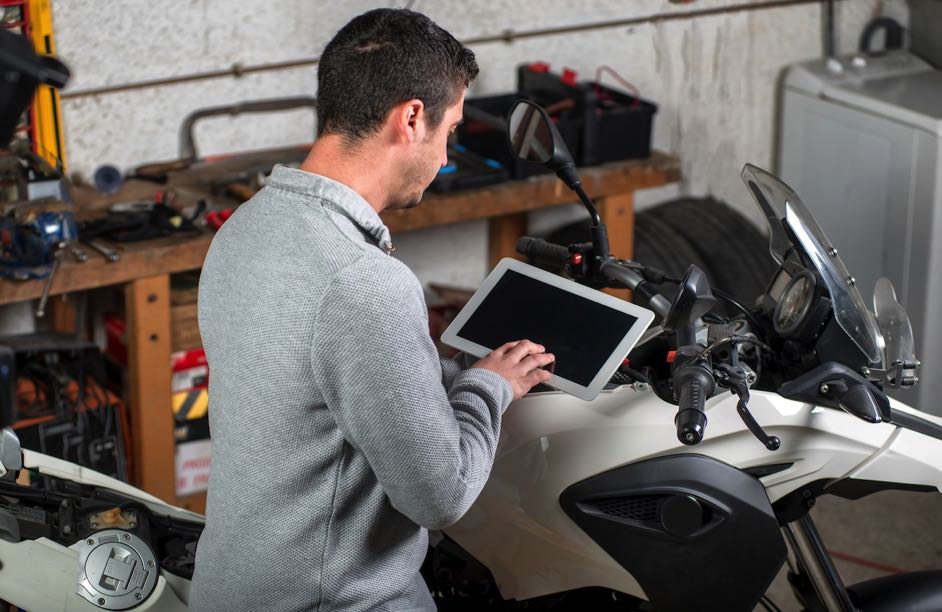 junger-mann-der-eine-tablette-nahe-bei-motorrad-verwendet
